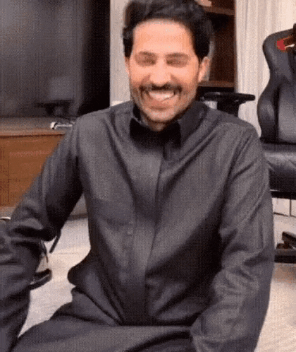 a man in a black shirt and mustache is sitting on the floor laughing .