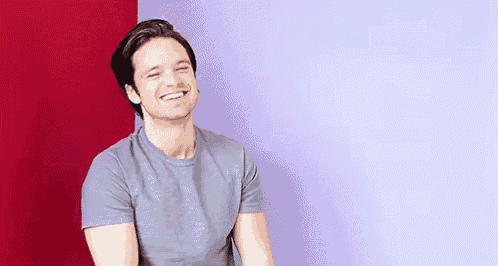 a man in a grey t-shirt is sitting in front of a red and purple wall .
