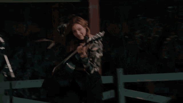 a girl in a camo jacket is singing into a microphone while holding a guitar
