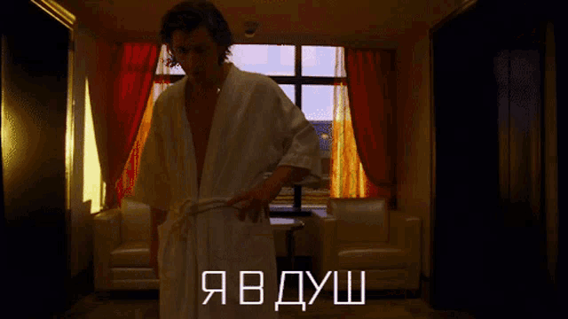 a man in a bathrobe is standing in a hallway with the words " я в душ " written above him