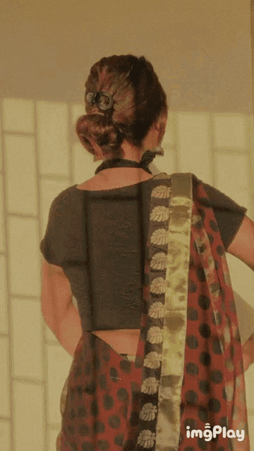 a woman wearing a gray blouse and a red polka dot saree is standing in front of a window