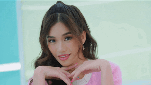 a woman in a pink sweater makes a heart shape with her hands