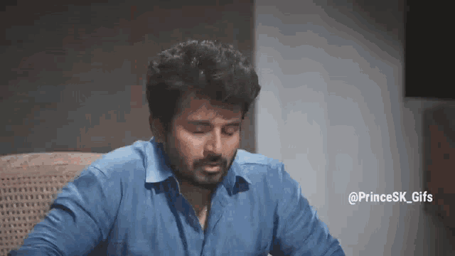 a man in a blue shirt is sitting in a chair with his eyes closed and his mouth open .
