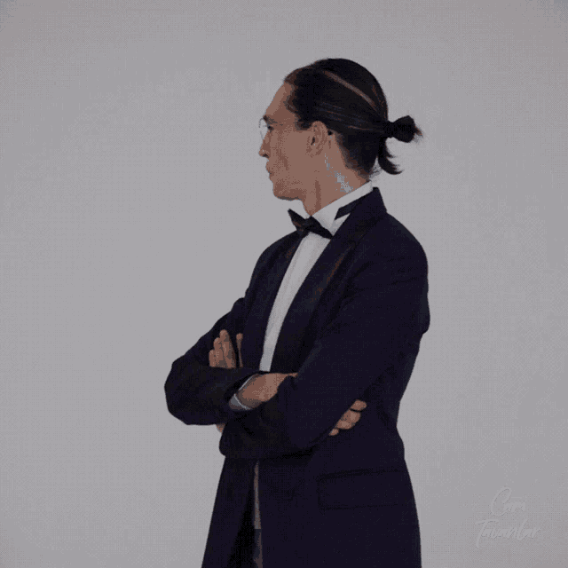 a man in a tuxedo is standing with his arms crossed in front of a white background that says " cami tavanlar "