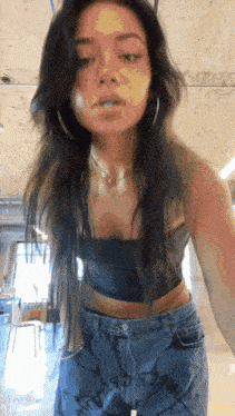 a woman wearing a black crop top and blue jeans has a tattoo on her lower leg