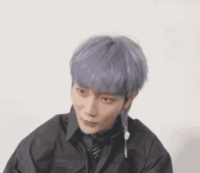 a young man with purple hair and earrings is sitting in front of a wall .