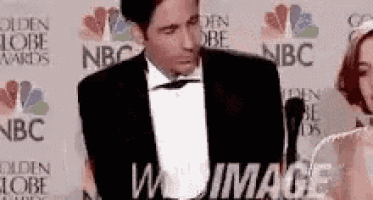 a man in a tuxedo is standing in front of a microphone at a golden globe awards event .