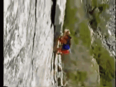 a woman is climbing up a cliff with a red and blue shirt on