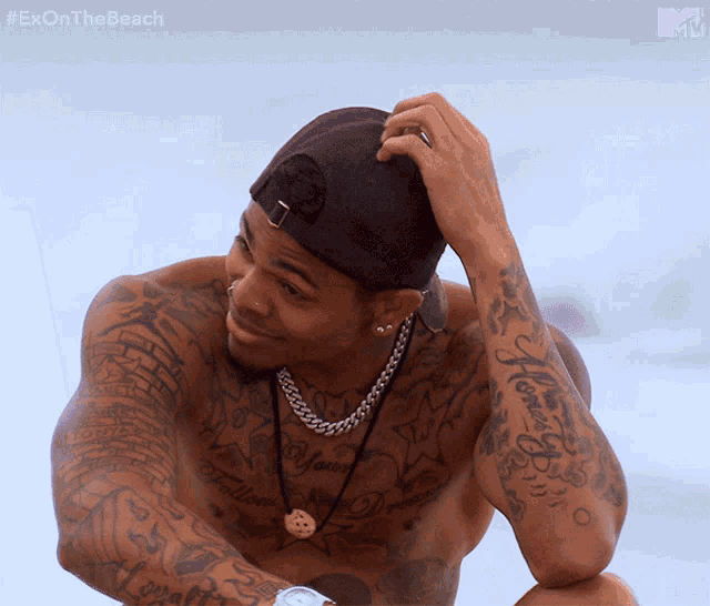 a shirtless man with a lot of tattoos on his arms and torso is on the beach