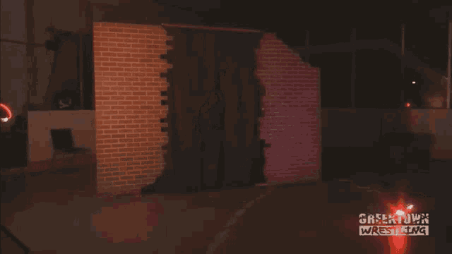 a man stands in front of a brick wall with the words greektown wrestling on the bottom
