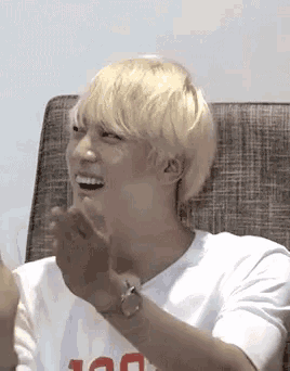 a young man with blonde hair is sitting on a couch laughing and clapping his hands .