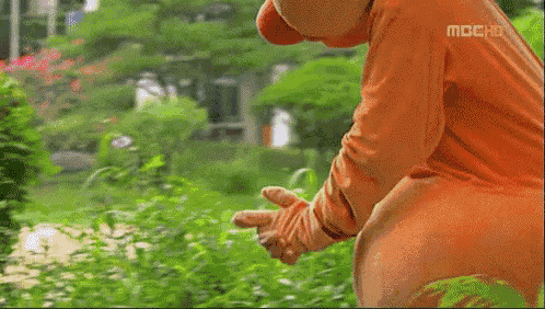 a baby in an orange outfit is standing in the grass with a man in a white shirt standing behind it .
