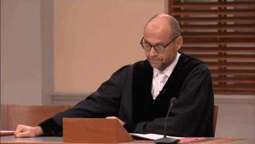 a man in a judge 's robe sits at a desk with a microphone in front of him