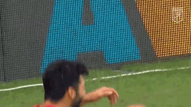 a man with a beard is standing on a soccer field in front of a sign that says a.