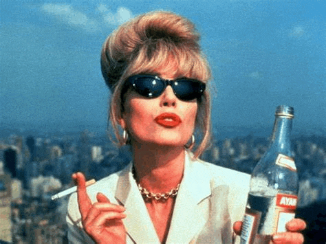 a woman wearing sunglasses is smoking a cigarette and holding a bottle of liquor .