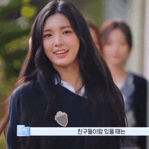 a girl with long black hair is smiling and wearing a sweater with a heart emblem on it