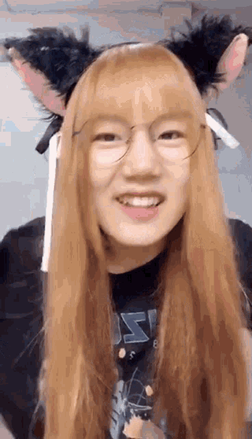 a girl with long blonde hair and cat ears is wearing glasses and a black shirt .