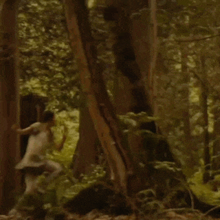 a woman in a white dress is running through a lush green forest .
