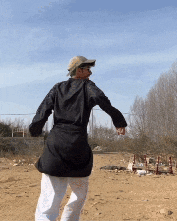 a man in a black shirt and white pants stands in a dirt field