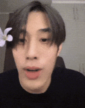 a young man with a flower in his hair is making a face .