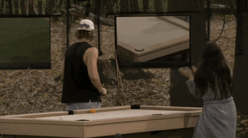 a man and a woman are playing a game of pool in the woods