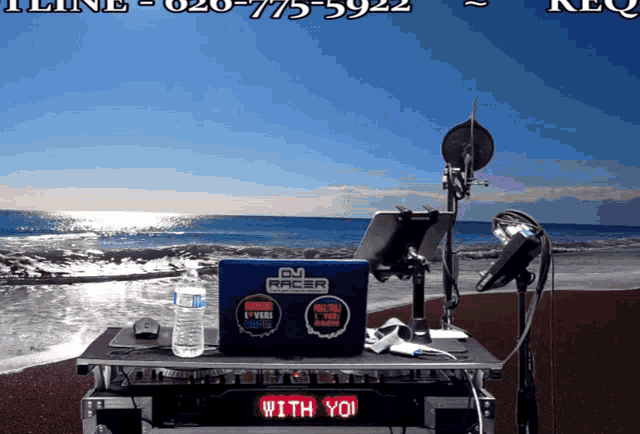 a dj racer laptop sits on top of a table in front of a beach