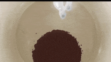 milk is pouring into a bowl of chocolate powder .
