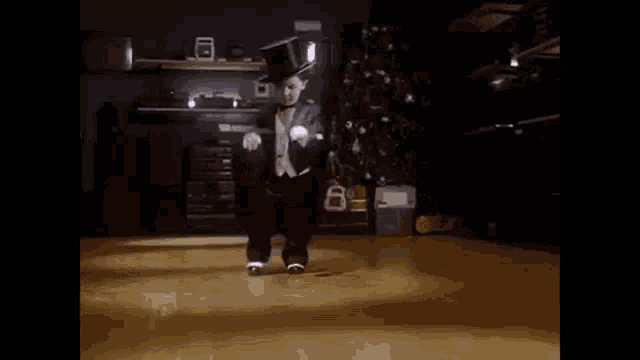 a little boy in a tuxedo and top hat is dancing on a wooden floor in a living room .