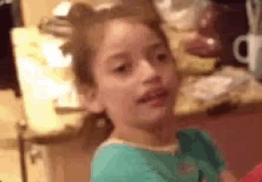 a young girl in a blue shirt is standing in front of a counter .