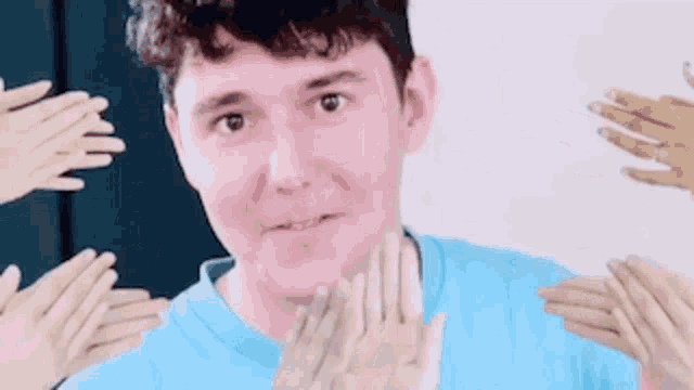a man in a blue shirt is surrounded by a group of hands .