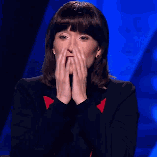 a woman covering her face with her hands in front of a blue backdrop