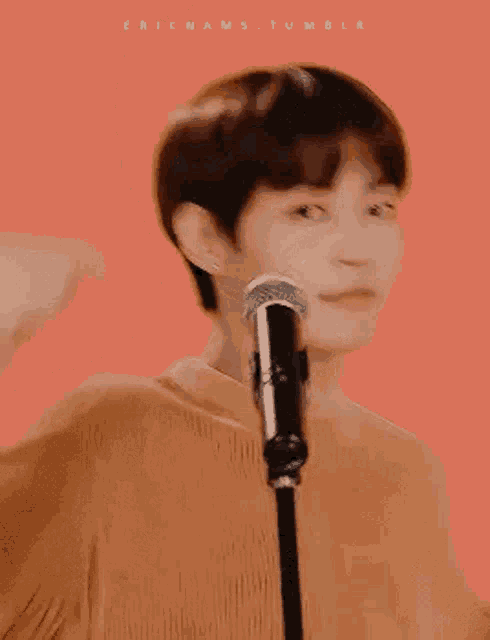 a young man is standing in front of a microphone making a heart shape with his hand .