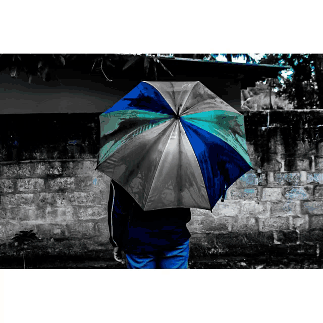 a person holding a colorful umbrella in front of a stone wall