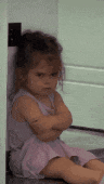 a little girl is sitting on the floor with her arms crossed and looking angry .