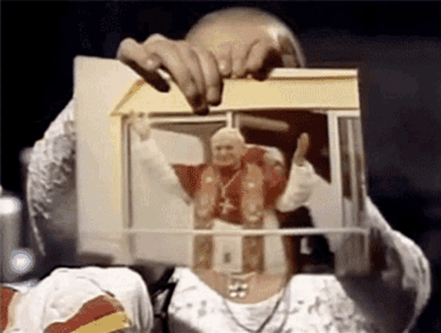 a man is holding a picture of a pope in a tiny house