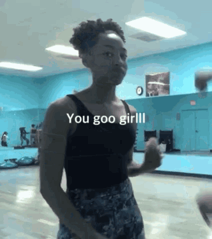 a woman in a black tank top is standing in a gym with the words `` you goo girl '' written on the bottom .