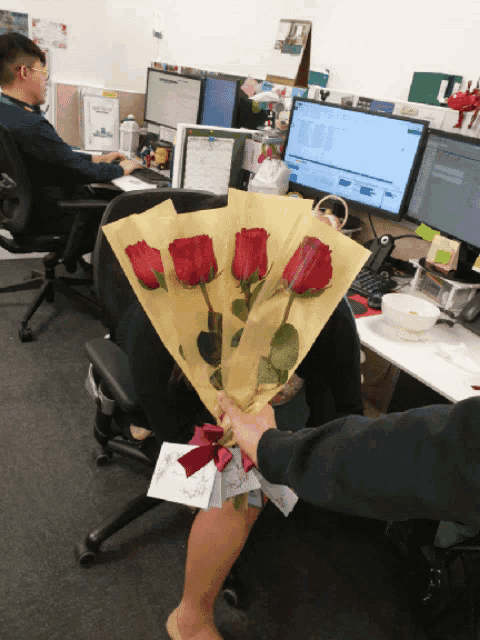 a person is holding a bouquet of red roses in front of a computer monitor