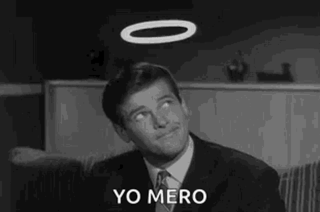 a man in a suit and tie is sitting on a couch with a halo on his head and the words `` yo mero '' .