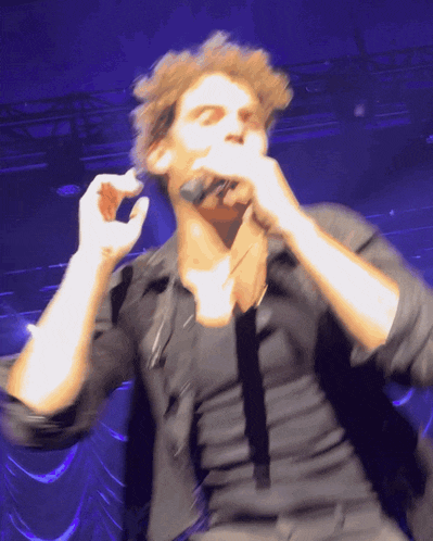 a man in a black shirt is singing into a microphone on a stage