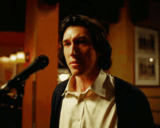 a man stands in front of a microphone with a picture on the wall behind him