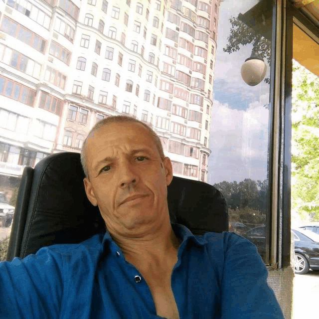 a man in a blue shirt sits in front of a building