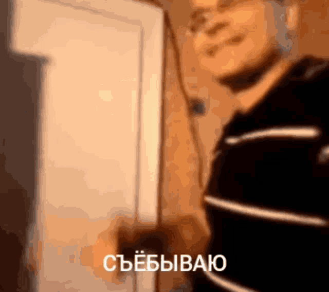 a man in a black and white striped shirt is standing in front of a door with russian writing on it .