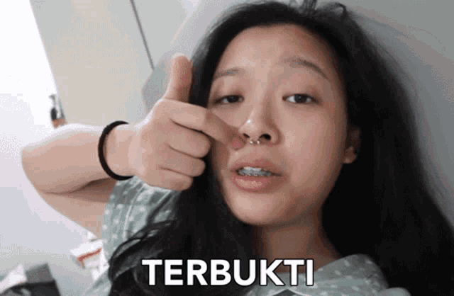 a woman with braces on her teeth is giving a thumbs up and the word terbukti is on the bottom