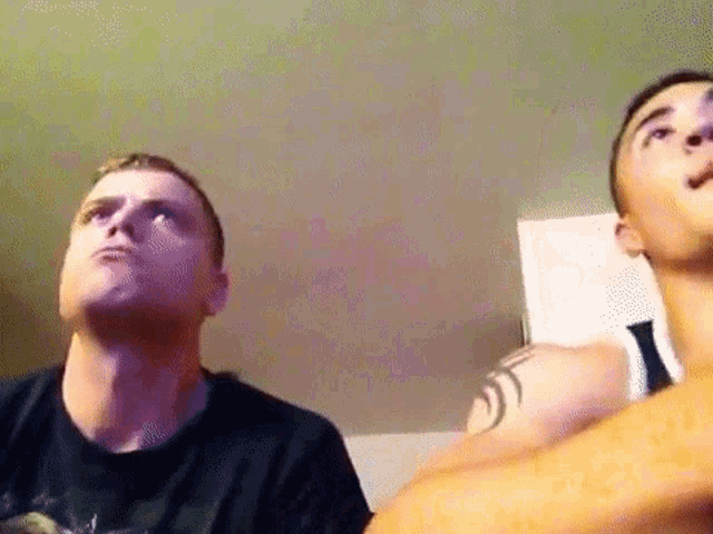 two men are looking up at the ceiling and one has a tattoo on his shoulder .