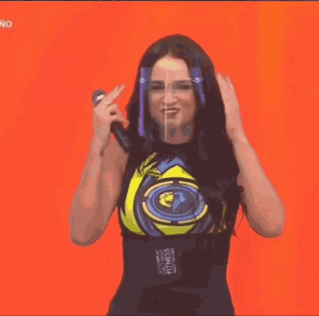 a woman wearing glasses and a black top is standing on a stage and holding her hair .