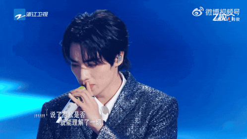a man singing into a microphone with chinese writing on the bottom