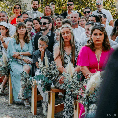 a woman in a pink dress sits in a crowd of people watching a wedding ceremony