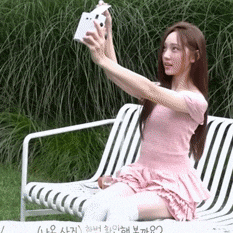 a woman in a pink dress is sitting on a lawn chair taking a selfie with a camera .