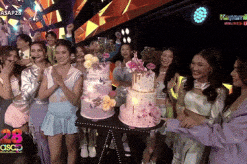 a group of people standing around a cake with the number 28 on it