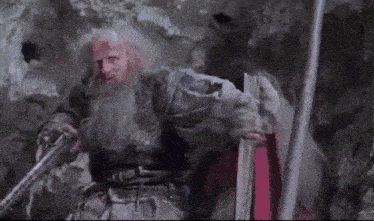 a man in a blue robe is standing on a rock holding a sword .